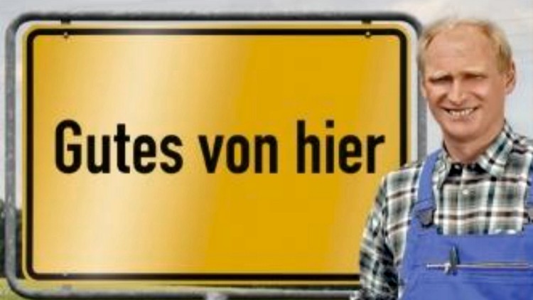 Gelbes Schild mit schwarzer Aufschrift „Gutes von hier“, Person in blauer Schürze hält Korb mit Kartoffeln vor einer Wiese.