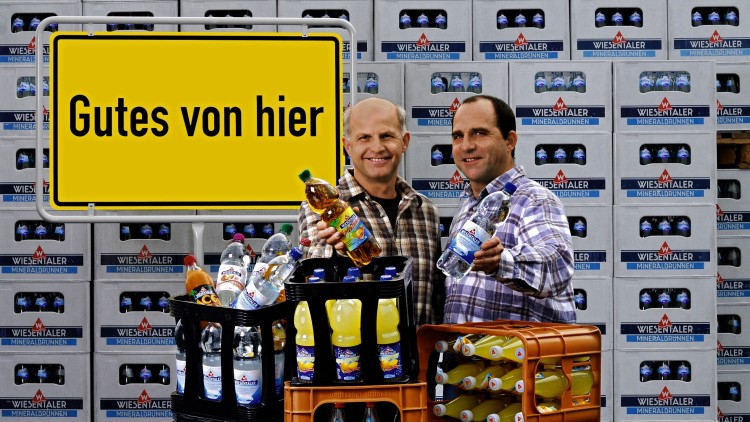 Zwei Personen stehen vor Getränkekästen der Marke WIESENTALER, ein Schild mit der Aufschrift Gutes von hier ist sichtbar.