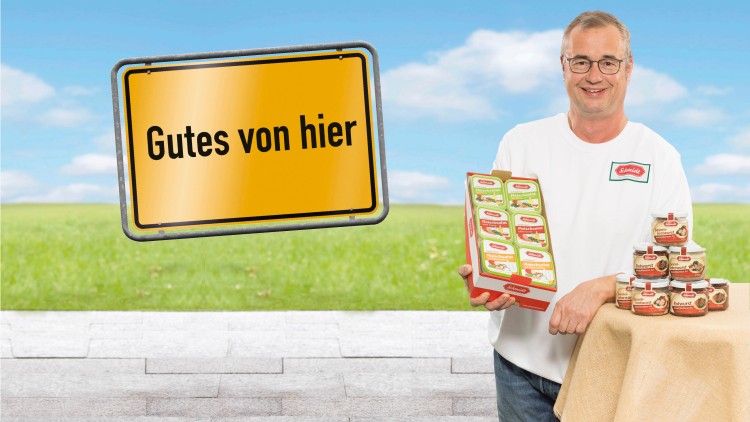 Ein gelbes Schild mit der Aufschrift „Gutes von hier“, daneben Präsentation von Konserven der Marke Schäfer mit Wurstprodukten.