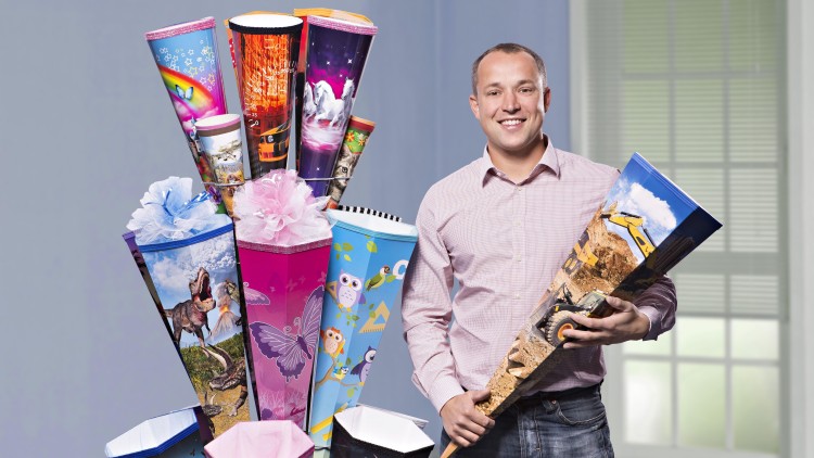 Mehrere bunte Schultüten mit verschiedenen Motiven, darunter Dinosaurier und Schmetterlinge, vor einem Fenster aufgestellt.