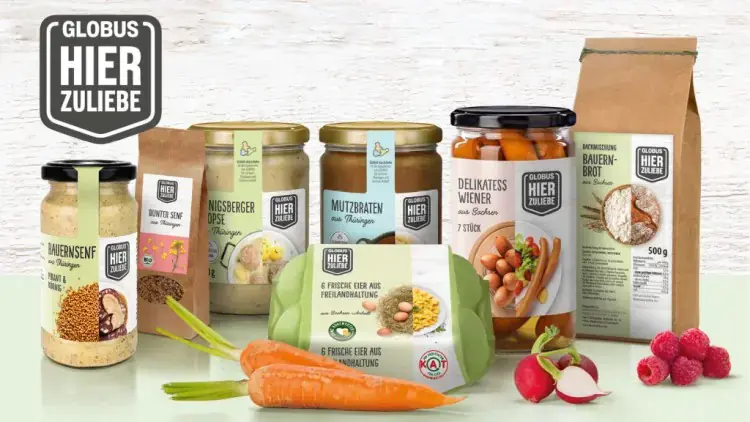 Produkte von GLOBUS HIER ZULIEBE wie Senf, Brot, Eier, Gemüse, eingelegte Würstchen und Glaswaren vor hellem Hintergrund.