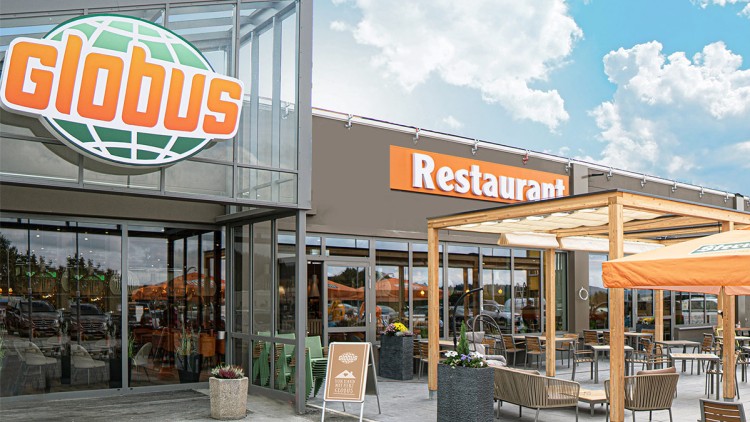 Eingangsbereich eines GLOBUS mit Glasfassade, darüber ein GLOBUS-Logo, daneben Restaurant-Schriftzug und Außenbestuhlung.