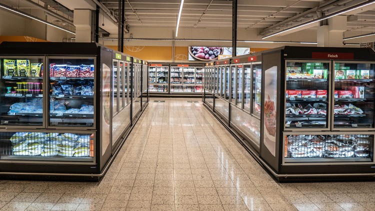 Gang mit beleuchteten Kühltruhen voller Tiefkühlprodukte in einem GLOBUS Markt, Beschilderung „Fleisch“ auf der rechten Seite.