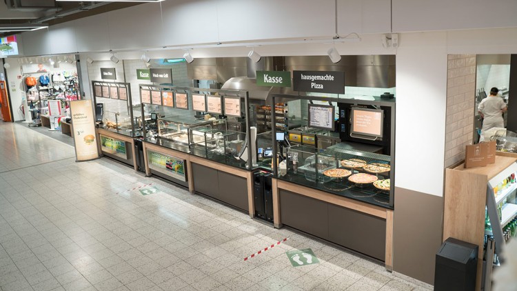 Verkaufstheke in einem GLOBUS Markt mit Schildern für „Frisch vom Grill“, „hausgemachte Pizza“ und sichtbaren Speisen.