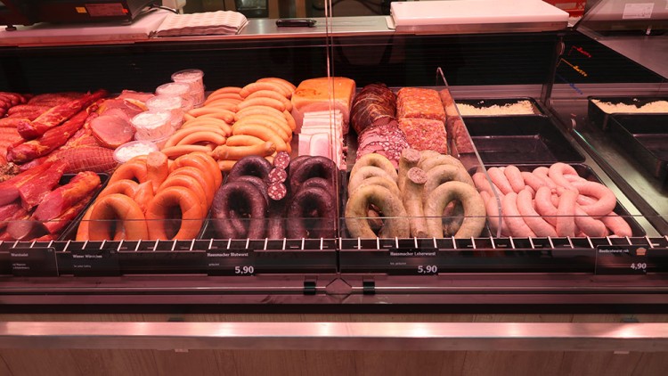 Verschiedene Wurstsorten, darunter Ringe, Scheiben und Brühwürste, liegen in einer gekühlten Theke mit Preisschildern.