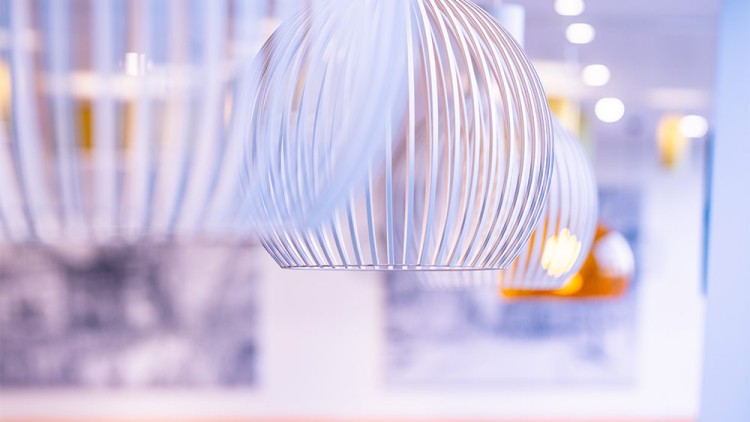 Weiße, filigrane Metalllampenschirme in Gitteroptik hängen von der Decke in einer hellen, unscharfen Innenraumkulisse.