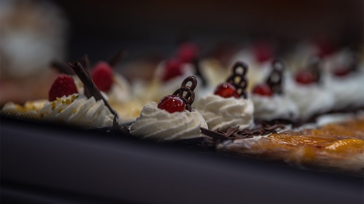 Kleine Törtchen mit Sahne, Schokodekor, Kirschen und Himbeeren in einer Theke.