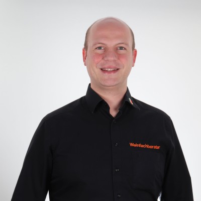 Person trägt ein schwarzes Hemd mit der Aufschrift „Weinfachberater“ in orange und eine blaue Jeans.