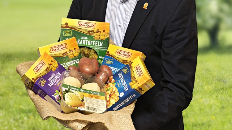 Mann in dunklem Sakko hält einen Leinenbeutel mit verschiedenen Friweika-Produkten wie Kartoffeln und Knödelmischungen.