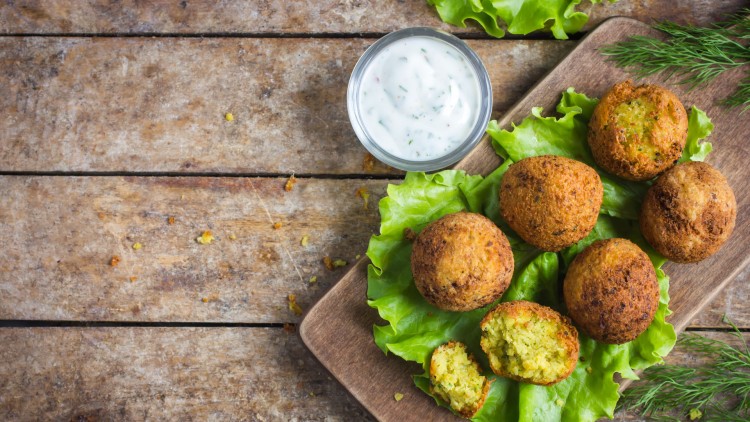 Sechs Falafel auf grünem Salat und einem Holzbrett, dazu ein Schälchen mit weißem Joghurt-Dip, auf einem Holztisch.