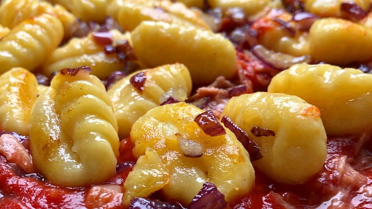 Nahaufnahme von gebräunten Gnocchi mit roten Zwiebelstücken in Tomatensauce.