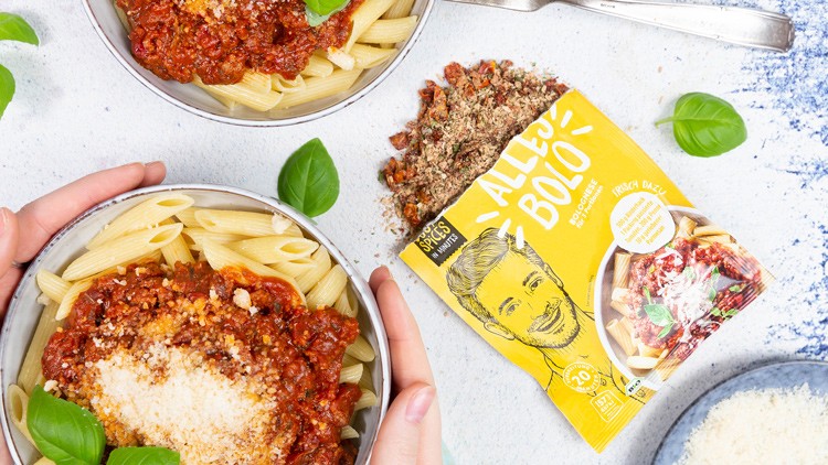 Zwei Schalen mit Penne, Tomatensoße und Parmesan, daneben gelbe Gewürzpackung „ALLES BOLO“ mit geöffneter Kräutermischung.